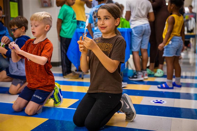 A girl wearing a brown shirt uses a spoon catapult